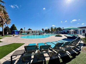 Ein Poolbereich mit Liegestühlen und Sonnenschirmen, umgeben von einer überdachten Sitzgelegenheit und einem Gebäude mit Beschilderung.