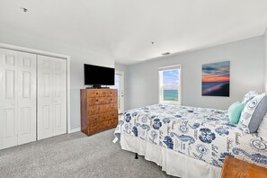A bedroom with a bed, dresser, TV, and two windows. - Ocean Views, Pools Hot Tub & Beach @Villa Capriani (North Topsail Beach)