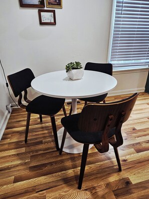 A round table with a potted plant, surrounded by four chairs with wooden frames and black cushions, on a wooden floor. - Cozy Greenville Home Near Hospitals & Downtown, Pet Friendly (Greenville)