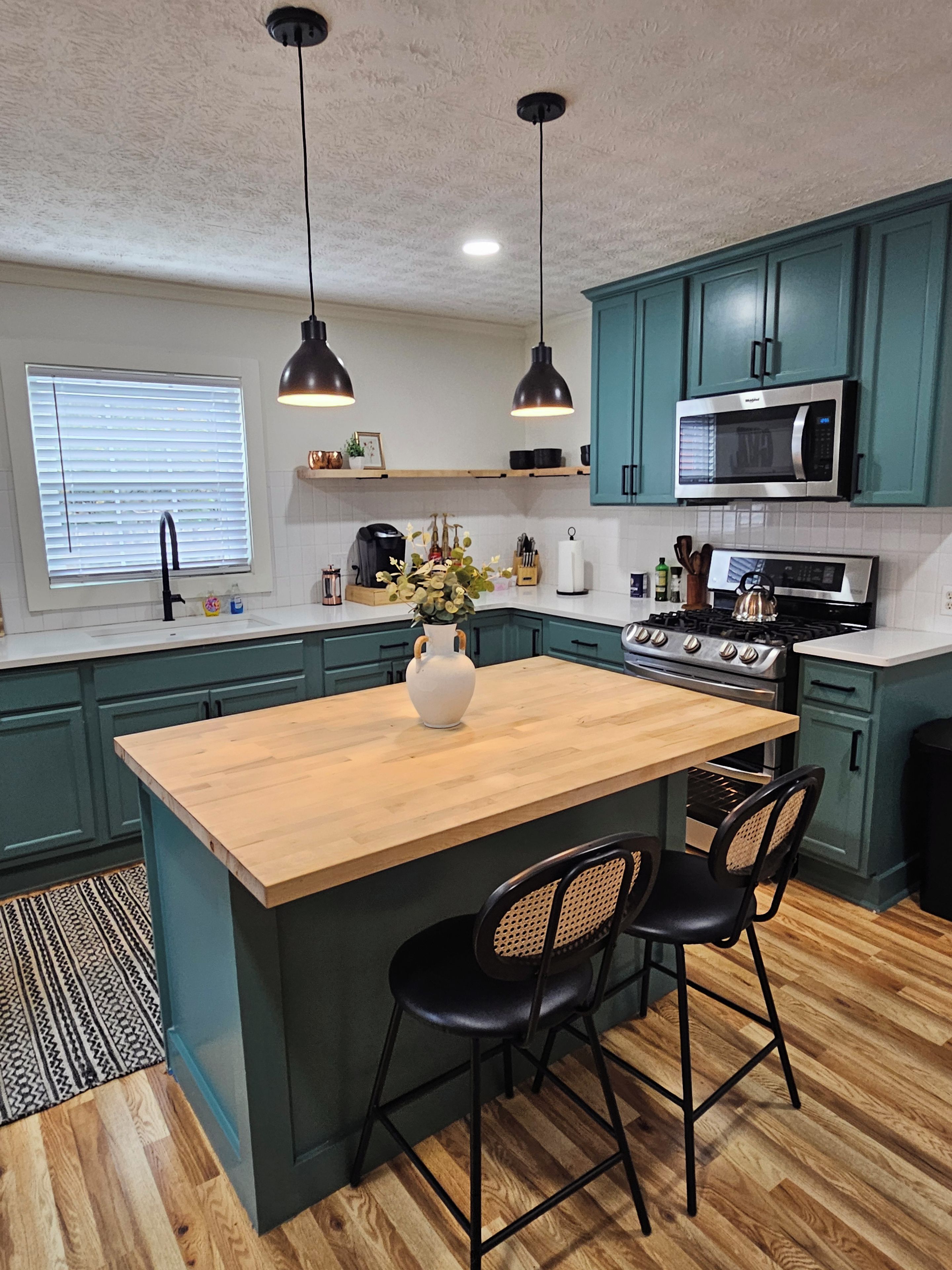 A kitchen with teal cabinets, a wooden island with two chairs, a stove, and a microwave.