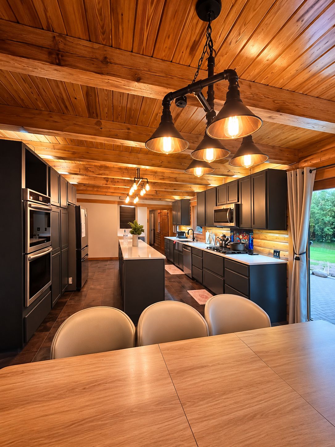 A modern kitchen with wooden ceiling beams, pendant lighting, and a central island with seating.