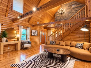 Interior de cabana de madeira com escada, mesa de centro redonda e tapete estampado com padrão de zebra.