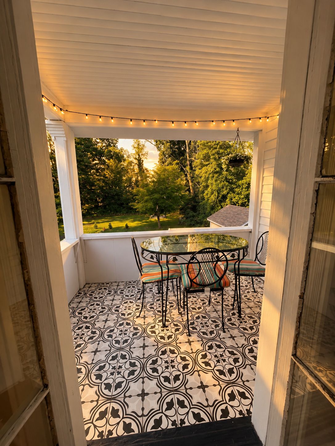 A covered patio with a table and chairs, a patterned floor, and a view of a garden.