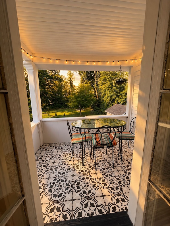 A covered patio with a table and chairs, a patterned floor, and a view of a garden.