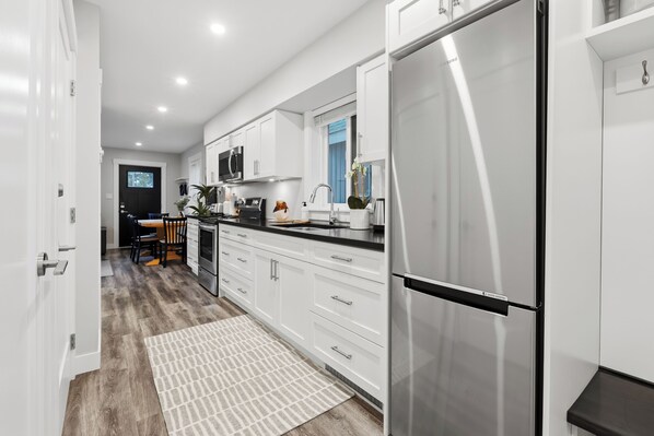 A modern kitchen with white cabinetry, stainless steel appliances, and a black countertop. - The Heron's Rest • Walk to Little Beach | Family Cottage + Bunk Room (Ucluelet)