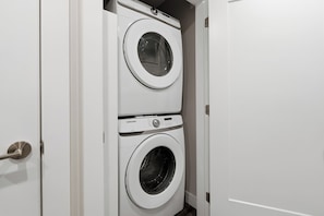 A white door with a silver handle leading to a laundry room containing two stacked washing machines. - The Heron's Rest • Walk to Little Beach | Family Cottage + Bunk Room (Ucluelet)
