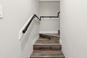 Eine Treppe mit Holzstufen und schwarzen Geländern, die zu einer Zwischenebene mit einer weißen Wand und einem Lichtschalter führt.