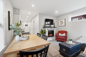 A modern living room with a fireplace, a dining area with a wooden table, and a red armchair. - The Heron's Rest • Walk to Little Beach | Family Cottage + Bunk Room (Ucluelet)