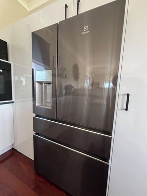A stainless steel refrigerator with a water dispenser, placed in a kitchen with white cabinets and a wooden floor. - Charming 3 Bdrm Parkside Qlder w Fabulous Deck. (Windsor)