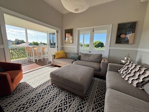 A living room with a sofa, ottoman, and a red armchair. There is a patterned rug on the floor. - Charming 3 Bdrm Parkside Qlder w Fabulous Deck. (Windsor)