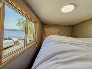 A bedroom with a bed, a window with a view of a lake and a parked car, and a door. - Waterfront Group Retreat | 2 Cabins | Sleeps 24 (Hammond)