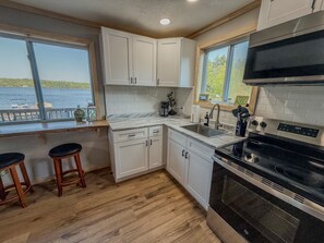 A kitchen with white cabinets, a black stove, and a view of the water outside. - Waterfront Group Retreat | 2 Cabins | Sleeps 24 (Hammond)