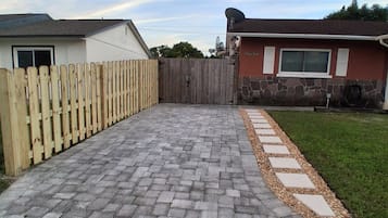 A paved driveway leading to a house with a wooden fence and a stone wall.