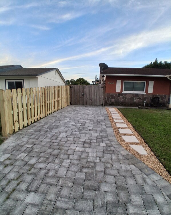 A paved driveway leading to a house with a wooden fence and a stone wall.