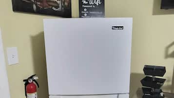A kitchen with a white refrigerator, a fire extinguisher, a wall-mounted sign, and a small table with a black tray.