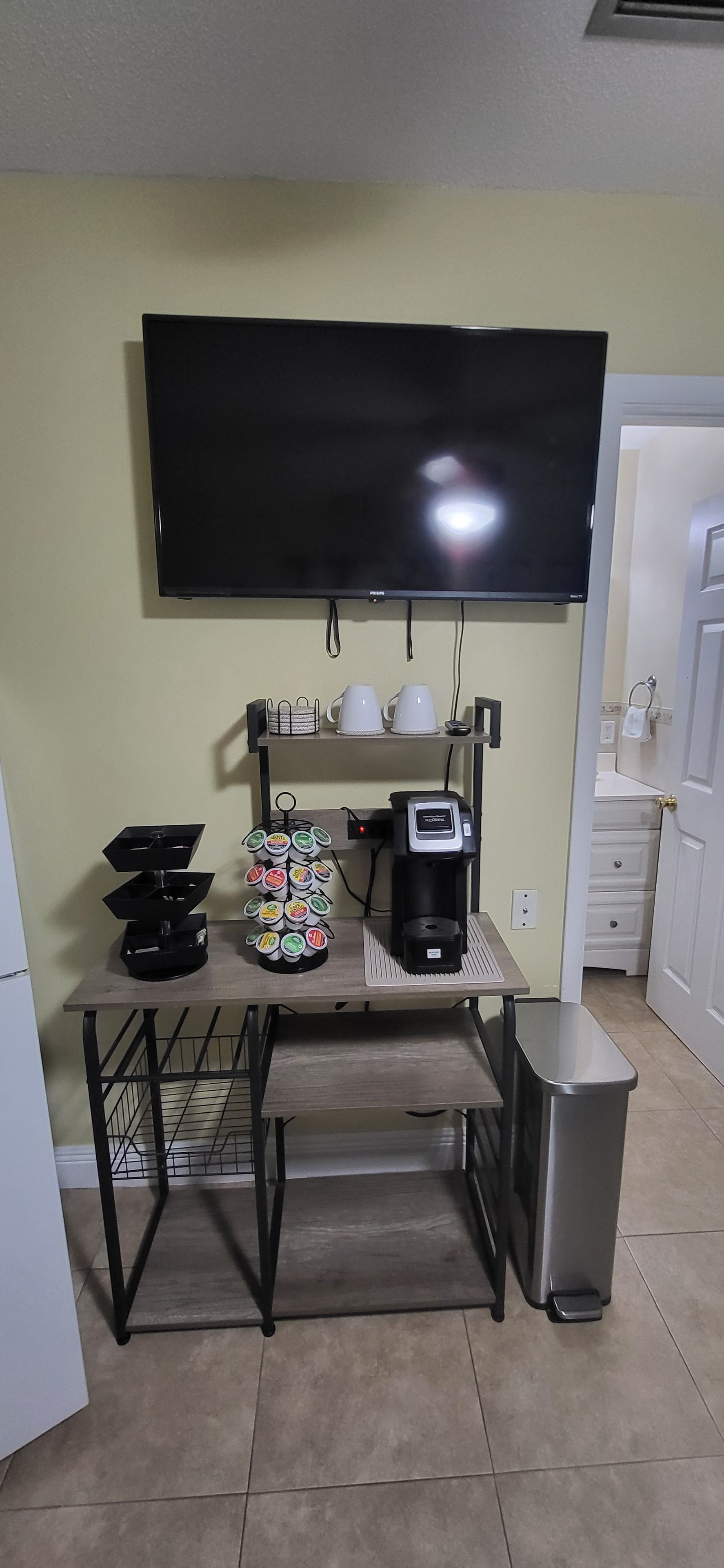 Une cuisine équipée d’un téléviseur à écran plat fixé au-dessus d’une table, d’une machine à café et d’une poubelle.