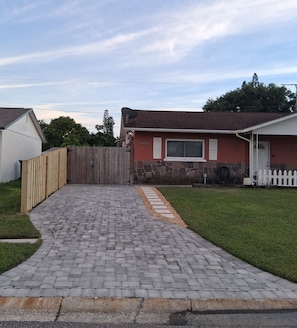 A residential property with a paved driveway leading to a wooden gate, a stone wall, and a white picket fence.