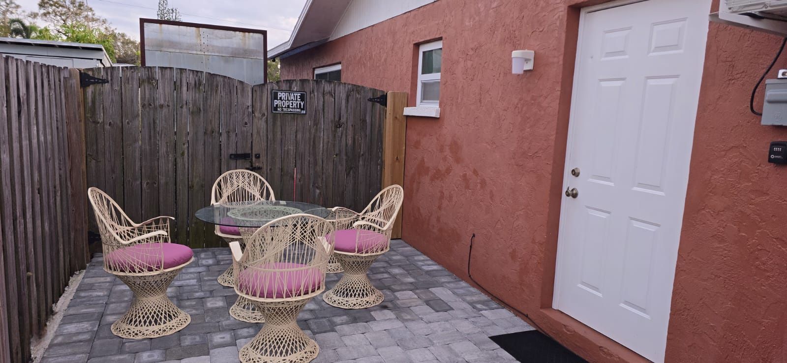 A private property with a wooden fence, a glass table with chairs, and a white door.
