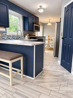 A modern kitchen with dark blue cabinets, a marble countertop, and a built-in island with a bench. - 5-bedroom Getaway w/ Private Pool, Arcade, Pool Table & More (Gastonia)