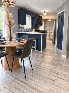 A modern kitchen with dark blue cabinets, a central island, and a dining area with a round table and chairs. - 5-bedroom Getaway w/ Private Pool, Arcade, Pool Table & More (Gastonia)