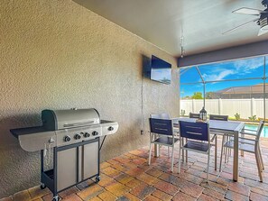 An outdoor patio with a grill, dining table, chairs, and a TV mounted on the wall. - Coastal Vibes and Pool Days- Cape Coral-5BR/3BA/ Sleep 12 (Cape Coral)