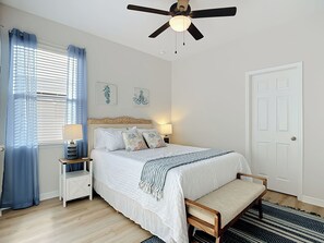 Ein Schlafzimmer mit einem Bett, Nachttischen, einem Deckenventilator und einer Tür.