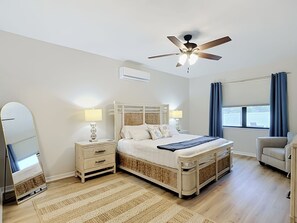 A hotel room with a bed, bedside tables, a ceiling fan, a window with curtains, and a mirror. - Coastal Vibes and Pool Days- Cape Coral-5BR/3BA/ Sleep 12 (Cape Coral)