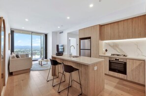 A modern kitchen with a central island, bar stools, a built-in oven, and a large window offering a city view. - Asteri at Broadbeach 10 min walk to the Beach, major entertainment downstairs (Broadbeach)