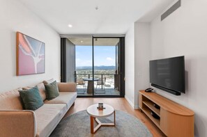 Ein modernes Wohnzimmer mit einer Couch, einem Couchtisch, einem Flachbildfernseher und einem Balkon mit Tisch und Stühlen.