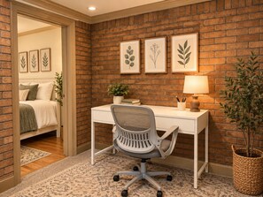 Ein Zimmer mit weißem Schreibtisch, einem Stuhl, einer Lampe, einem Blumentopf und gerahmten Pflanzenbildern an der Wand.