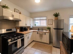 A modern kitchen with stainless steel appliances, white cabinetry, and a window with blinds. - Modern Rockford Apartment (Rockford)