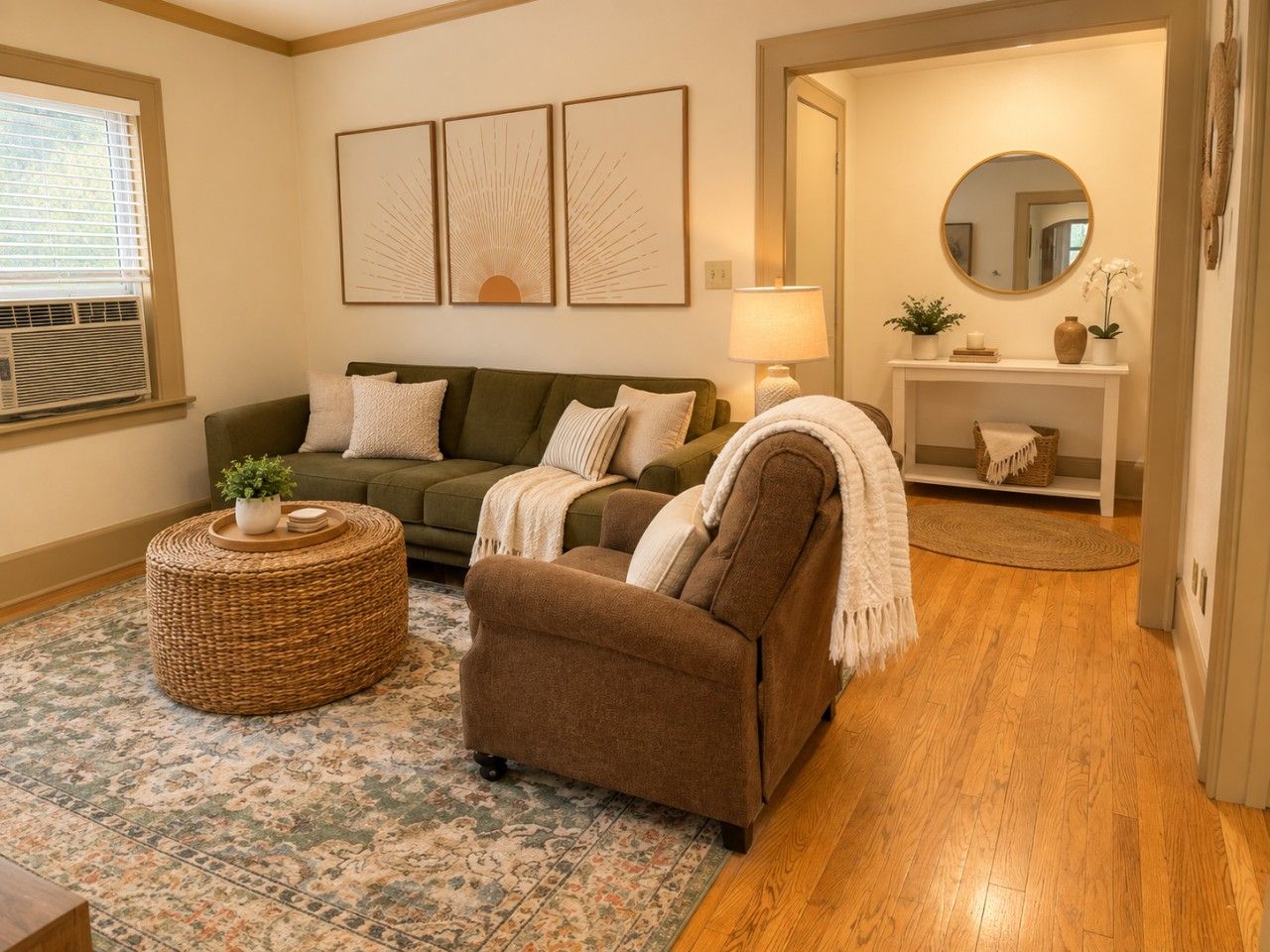 Un salon avec un canapé vert, un fauteuil marron, un pouf rond en osier et un tapis à motifs.