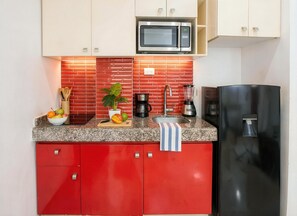 A kitchen with red cabinets, a stainless steel refrigerator, a microwave, a coffee maker, and a fruit bowl. - Queen Bed, Rooftop Pool, Quiet Street · Sleeps 4 · Beach & 5th Ave 10 Min Walk (Playa del Carmen)