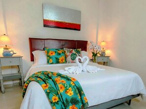 Ein Hotelzimmer mit einem Bett, zwei Nachttischen, einer Ablagefläche und einem Wandkunstwerk, sowie einer blumigen Tagesdecke.