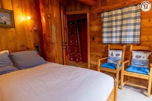 A wooden cabin room with a bed, two chairs with blue cushions, a plaid curtain, and a wall-mounted lamp. - Les Abeillos - Le Marmotton (BONNEVAL SUR ARC)