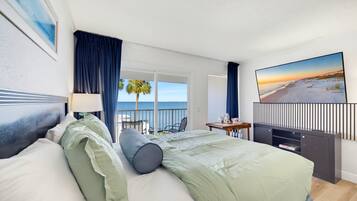 Ett hotellrum med en säng, ett skrivbord, en stol, en TV och en balkong med utsikt över havet.