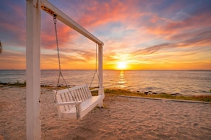 Eine Strandansicht mit einer Schaukelstuhlsitzgelegenheit und einem Sonnenuntergang über dem Ozean.