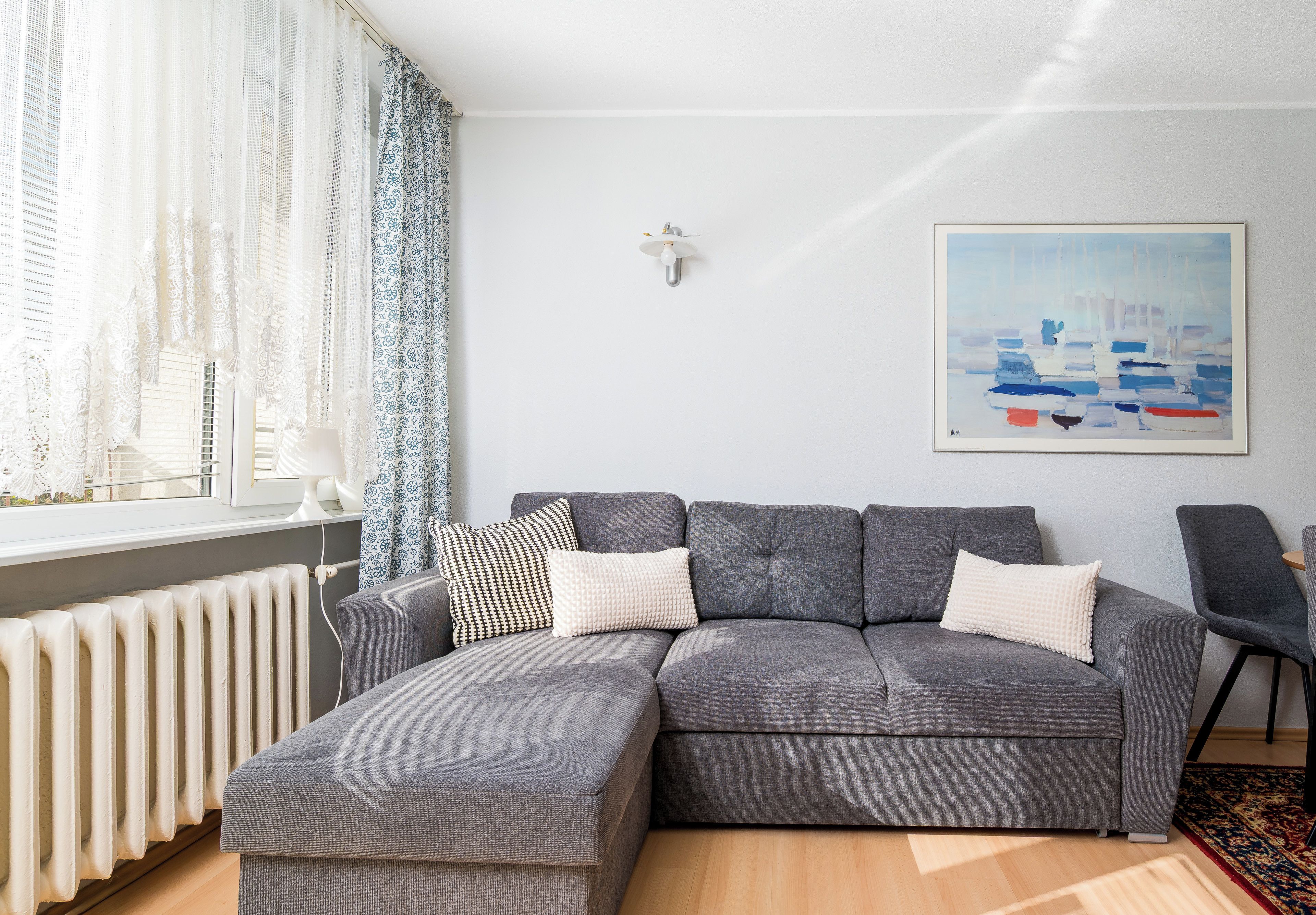 Un salon moderne avec un canapé gris, des coussins à motifs, un radiateur blanc et un tableau accroché au mur.