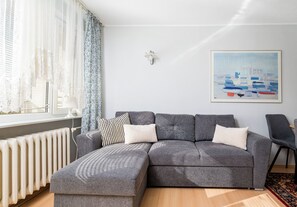 Ein modernes Wohnzimmer mit einem grauen Sofa, gemusterten Kissen, einem weißen Heizkörper und einem Bild an der Wand.