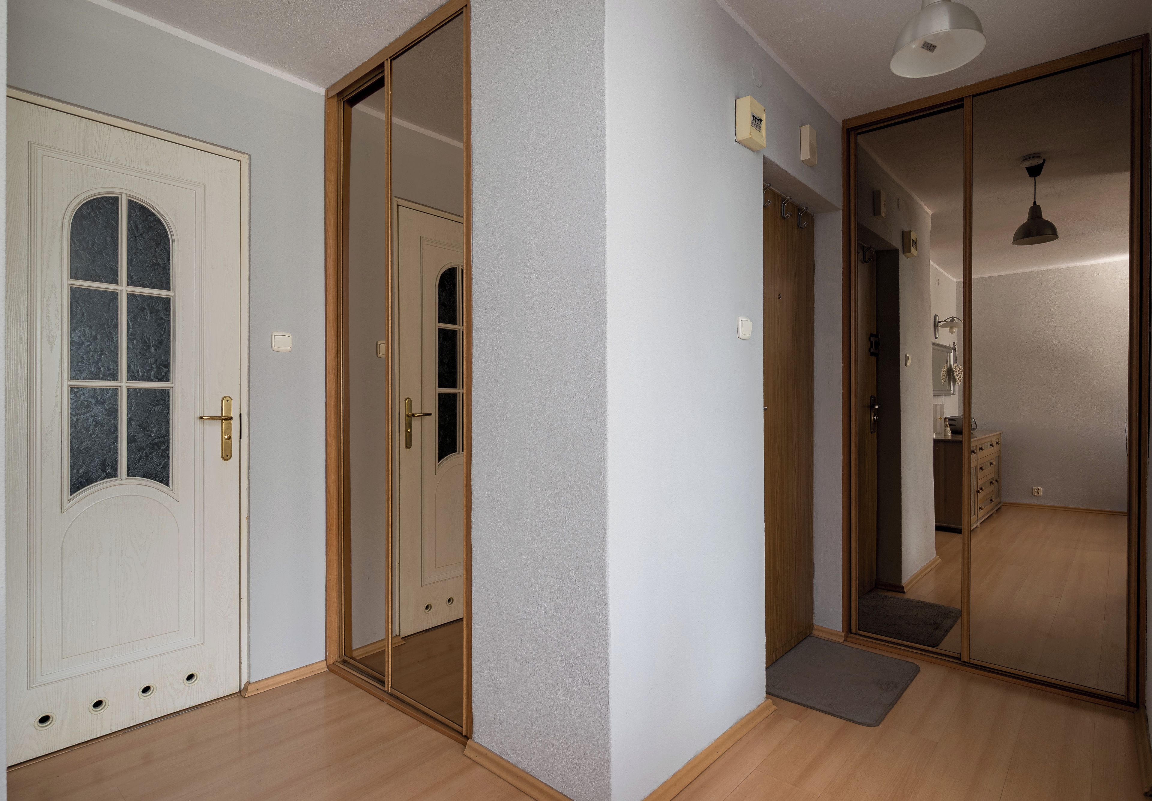 Un couloir doté d’un plancher en bois, d’une porte blanche avec un panneau de verre et d’une porte coulissante avec un miroir.
