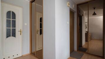 Un couloir doté d’un plancher en bois, d’une porte blanche avec un panneau de verre et d’une porte coulissante avec un miroir.