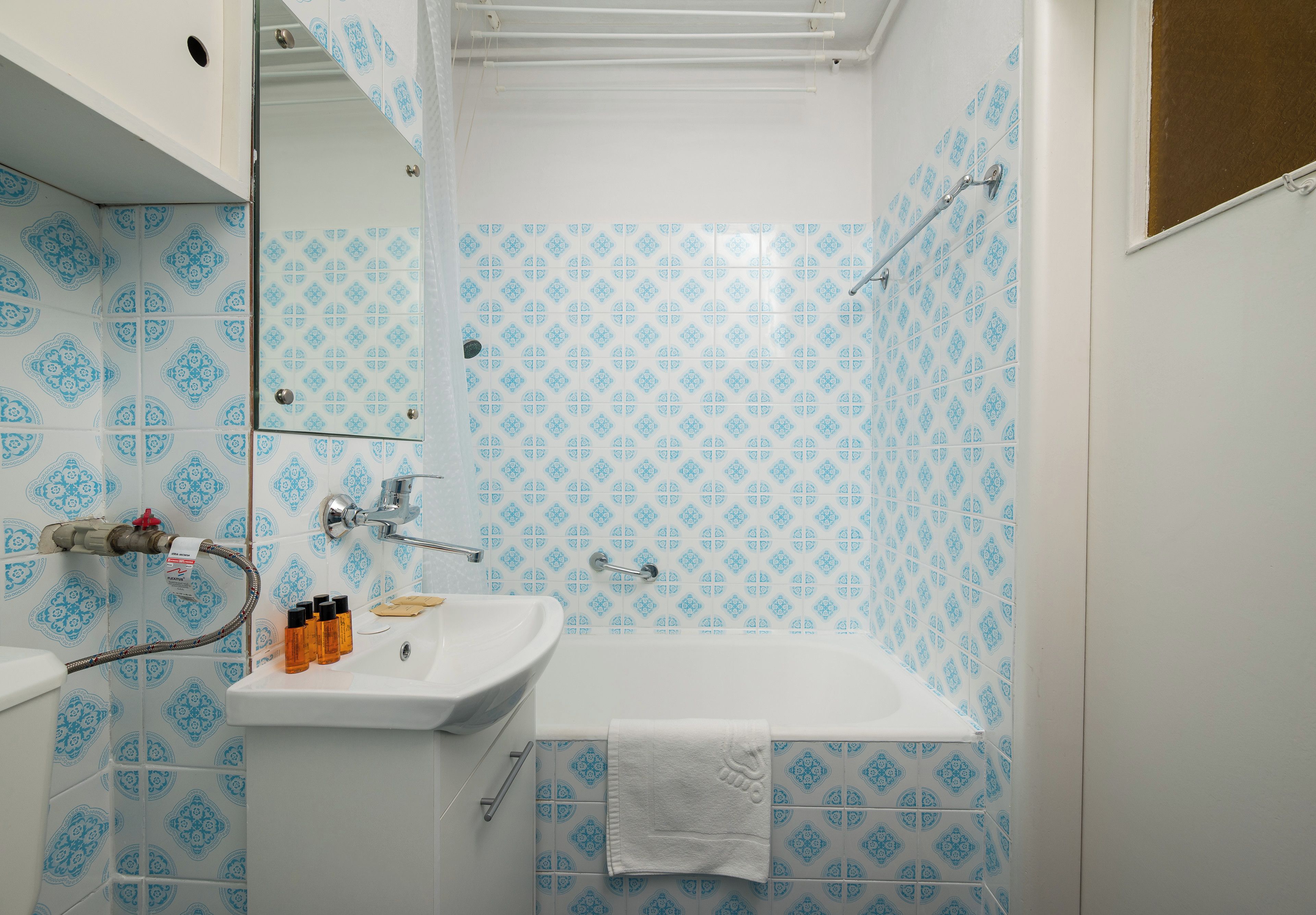 Un baño con un lavabo blanco, un espejo, una ducha con puerta de vidrio y azulejos con diseño azulado.