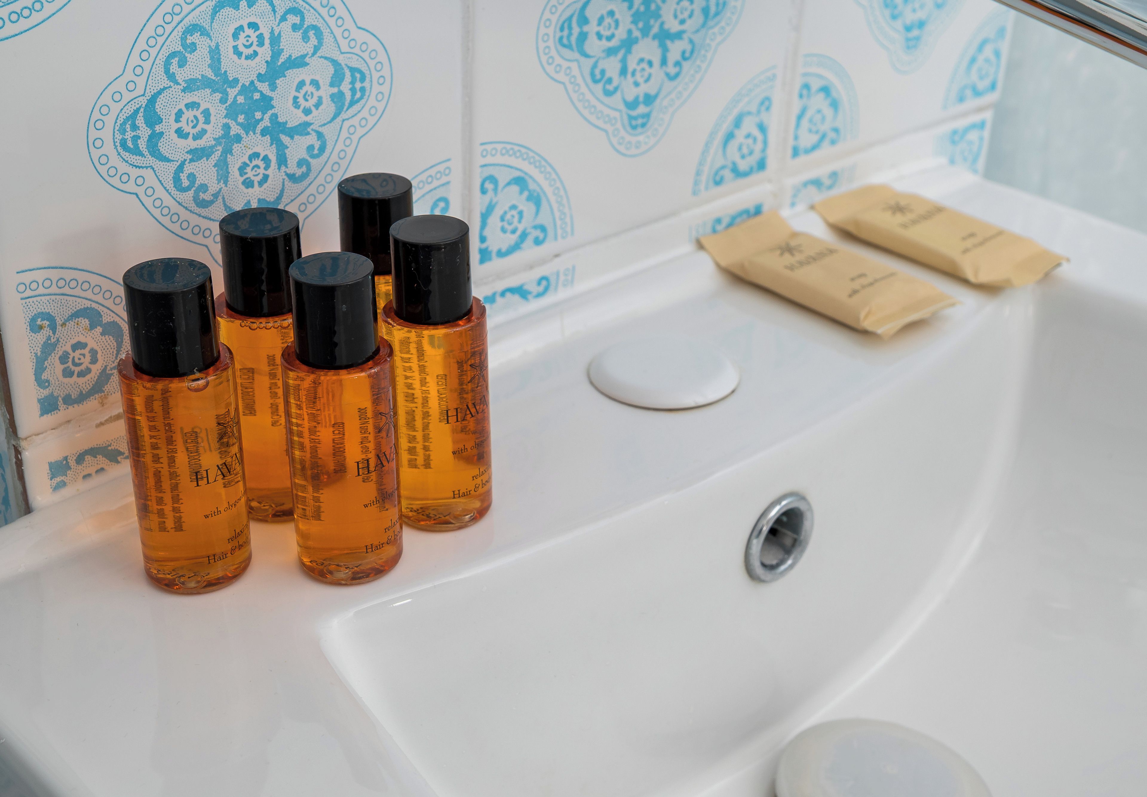 Un lavandino in bagno con diverse bottiglie di prodotti per la cura dei capelli e due piccoli pacchetti marroni sul bordo.