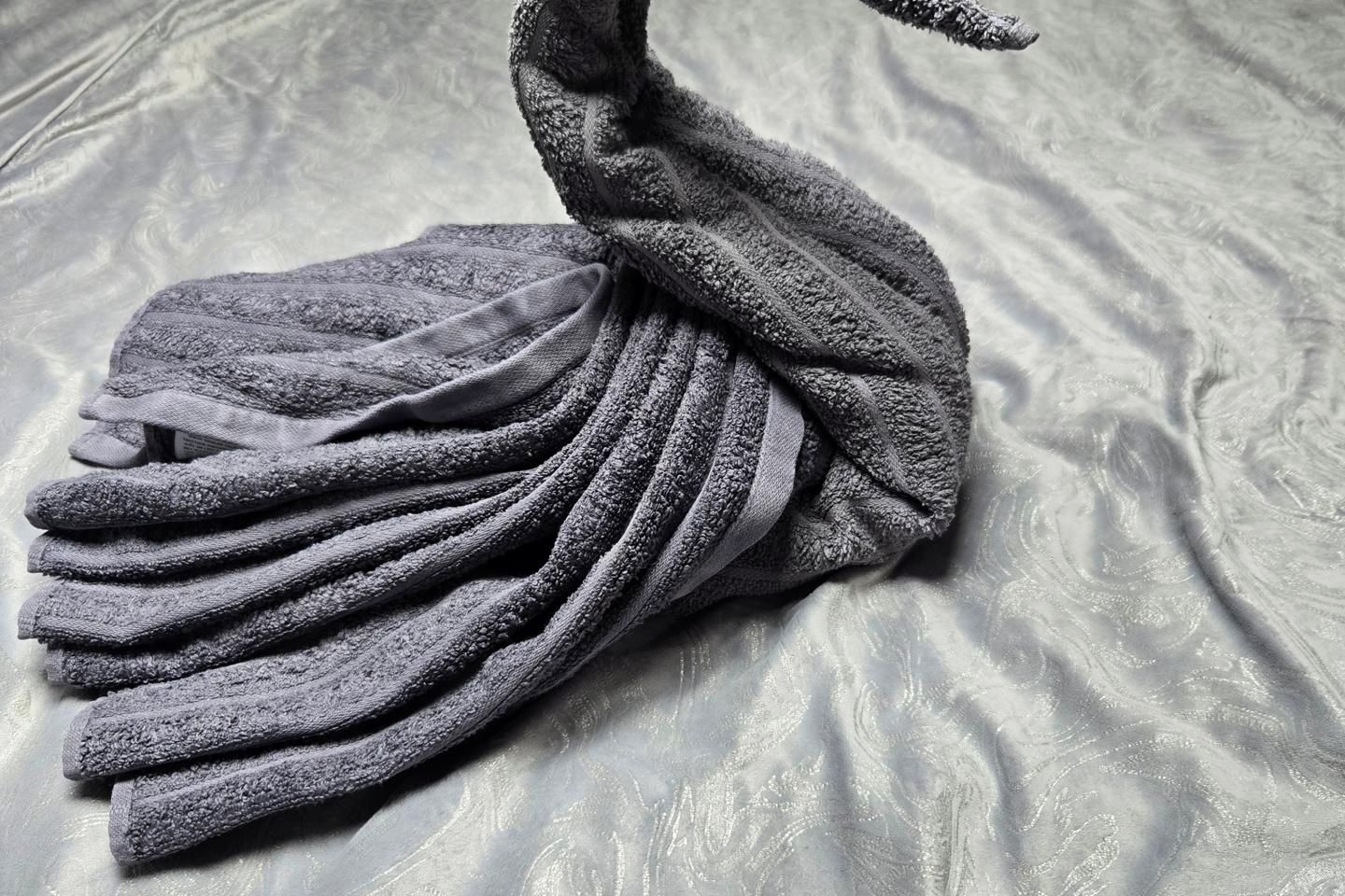 Une serviette pliée, dont la surface est texturée, posée sur un tissu à motifs ondulés.