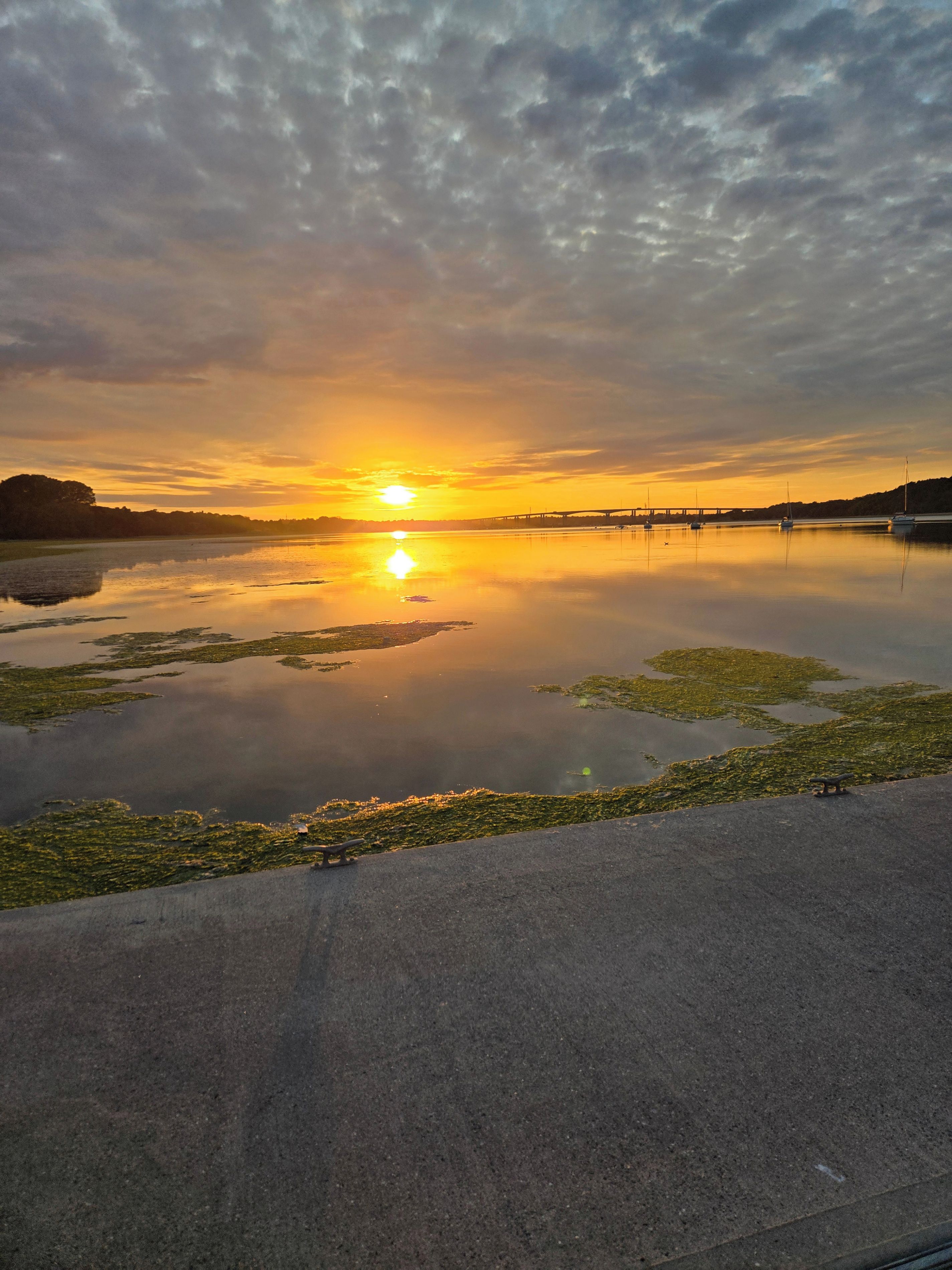 A sunset over a calm body of water with a bridge in the distance.
