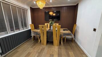 A dining area with a wooden table, chairs, a chandelier, and a television on the wall.