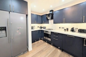 A modern kitchen with dark cabinets, a stainless steel refrigerator, a microwave, and a gas stove. - House Sleeps 6 with Parking (Louth)