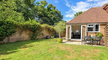 Un jardin avec une terrasse, une table et des chaises, un jardinier en forme de bac et une clôture en bois.