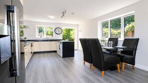 Une cuisine moderne avec un coin repas, comprenant un lave-linge encastré, une horloge et de grandes fenêtres.