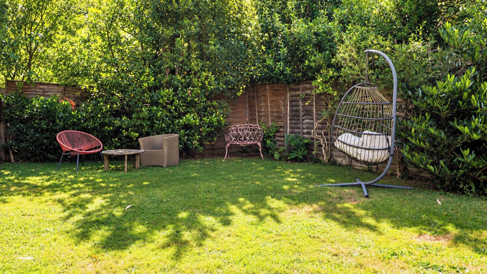 A backyard with a grassy lawn, a wooden fence, and three wicker chairs.